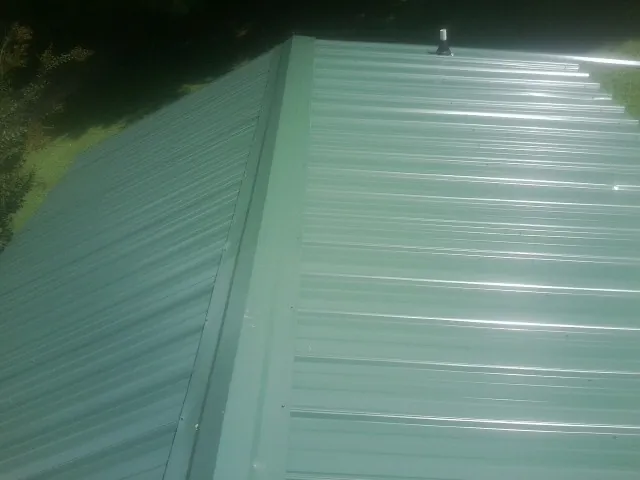 New green metal panels meeting at the ridge of a roof — Flat Roof Repair work by our crew in Sheldon