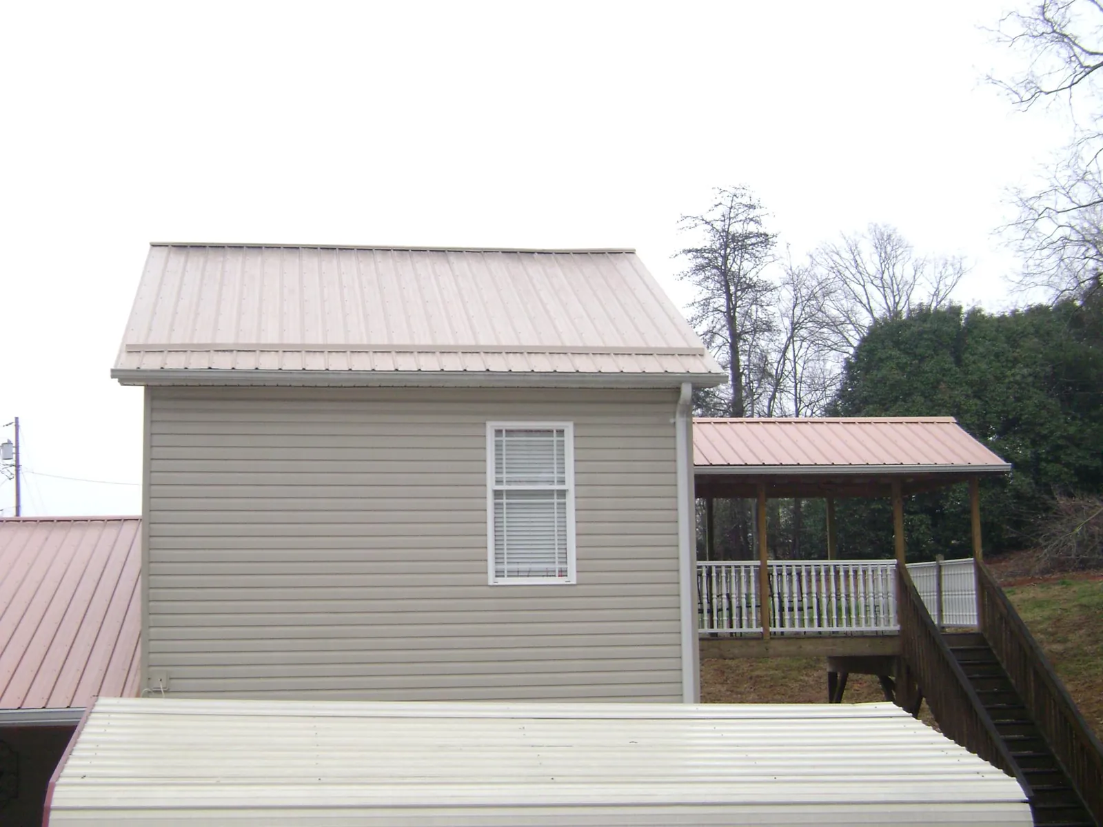 Tan metal roofs on a two story addition and attached porch, from a Roof Replacement job in Sheldon